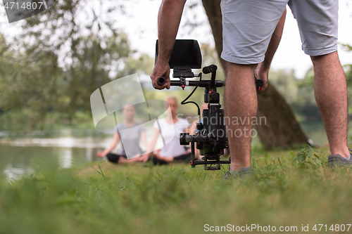 Image of young videographer recording while woman doing yoga exercise