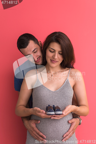 Image of young pregnant couple holding newborn baby shoes