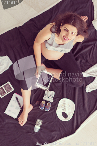 Image of top view of pregnant woman checking list of baby clothes