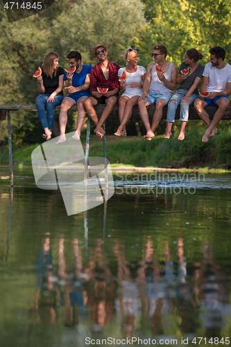 Image of friends enjoying watermelon while sitting on the wooden bridge