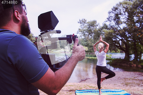 Image of young videographer recording while woman doing yoga exercise