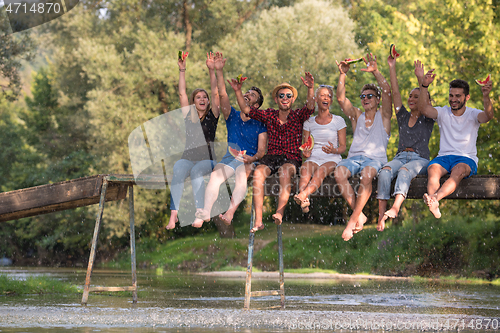 Image of friends enjoying watermelon while sitting on the wooden bridge