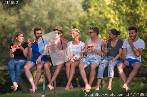 Image of friends enjoying watermelon while sitting on the wooden bridge