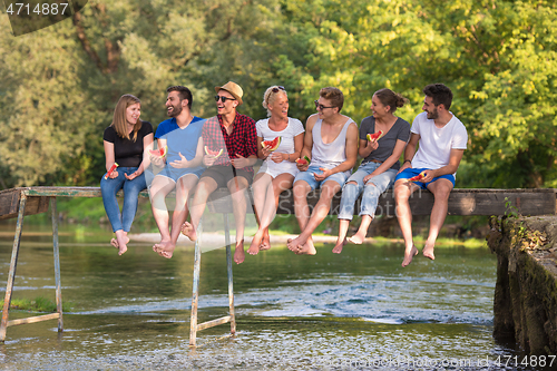 Image of friends enjoying watermelon while sitting on the wooden bridge