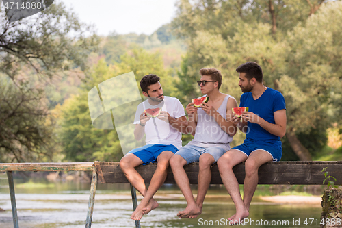 Image of men enjoying watermelon while sitting on the wooden bridge