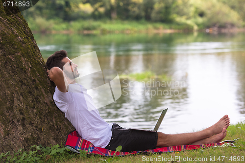 Image of man using a laptop computer on the bank of the river