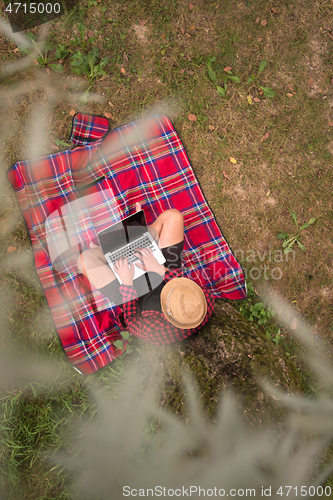 Image of top view of man using a laptop computer under the tree