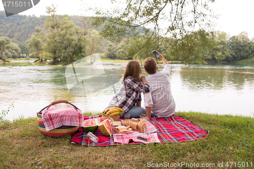 Image of Couple taking a selfie by mobile phone while enjoying picnic tim