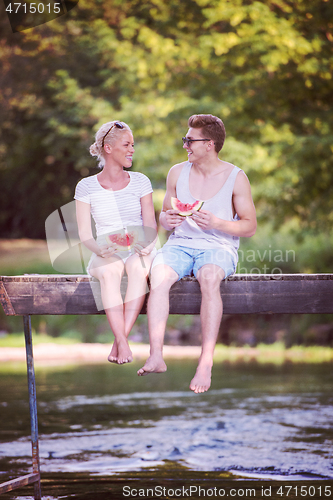 Image of couple enjoying watermelon while sitting on the wooden bridge