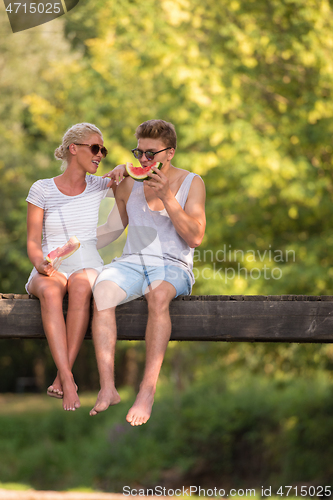 Image of couple enjoying watermelon while sitting on the wooden bridge