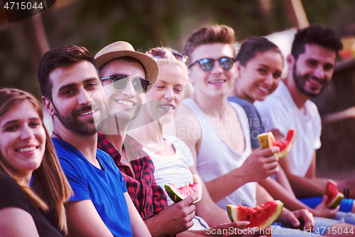 Image of friends enjoying watermelon while sitting on the wooden bridge