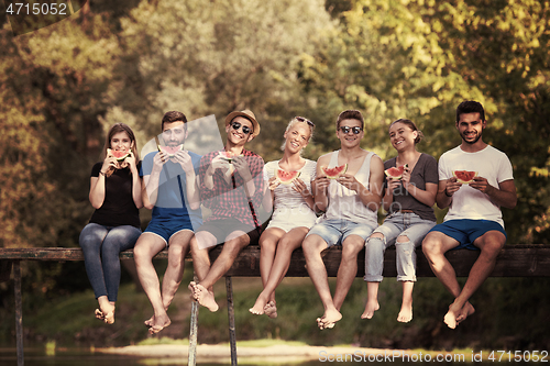 Image of friends enjoying watermelon while sitting on the wooden bridge