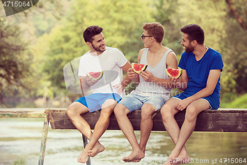 Image of men enjoying watermelon while sitting on the wooden bridge