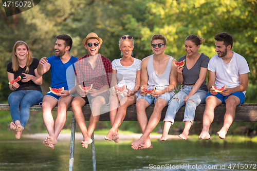 Image of friends enjoying watermelon while sitting on the wooden bridge