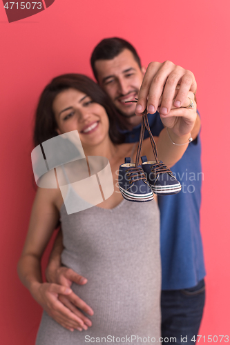 Image of young pregnant couple holding newborn baby shoes