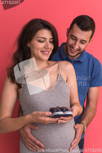 Image of young pregnant couple holding newborn baby shoes