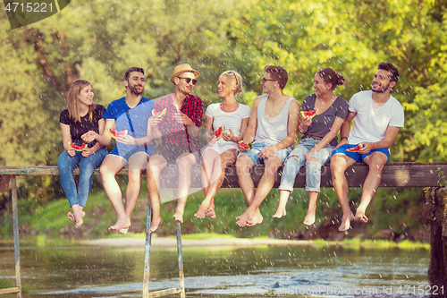 Image of friends enjoying watermelon while sitting on the wooden bridge