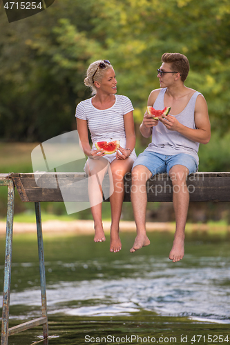 Image of couple enjoying watermelon while sitting on the wooden bridge