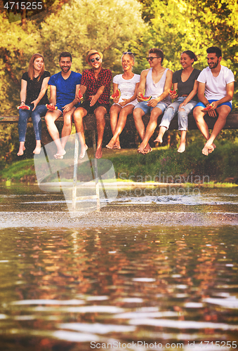 Image of friends enjoying watermelon while sitting on the wooden bridge