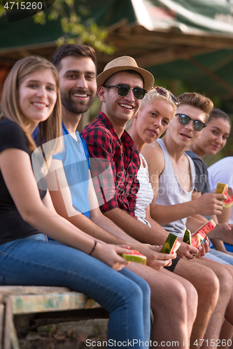 Image of friends enjoying watermelon while sitting on the wooden bridge