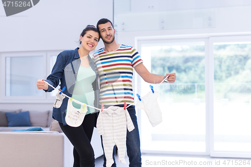 Image of young couple holding baby bodysuits at home