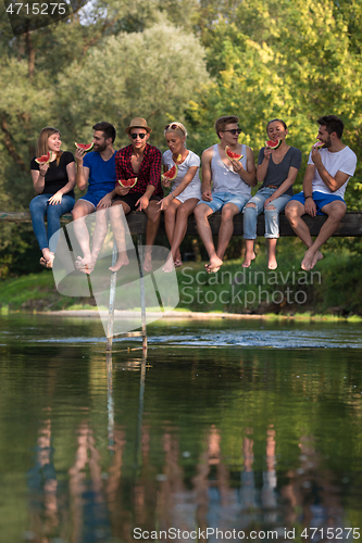 Image of friends enjoying watermelon while sitting on the wooden bridge