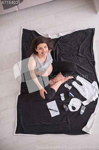 Image of top view of pregnant woman checking list of baby clothes