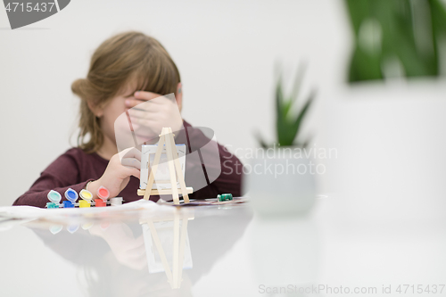 Image of little girl painting on canvas and hiding face