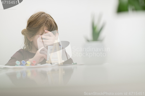 Image of little girl painting on canvas and hiding face