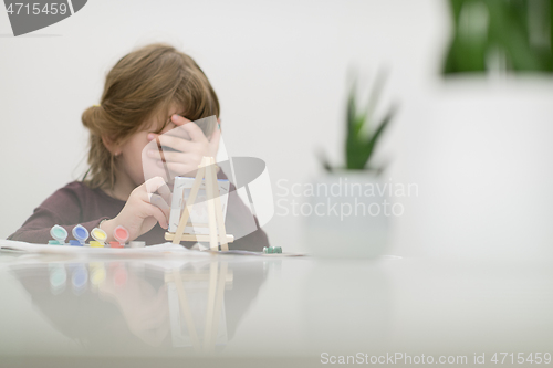 Image of little girl painting on canvas and hiding face