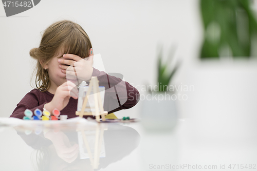 Image of little girl painting on canvas and hiding face