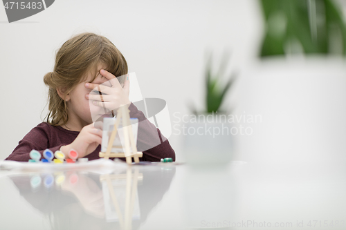 Image of little girl painting on canvas and hiding face