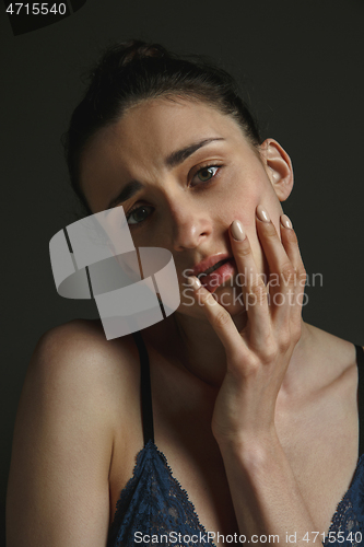 Image of Half-length portrait of young sad woman on dark studio background