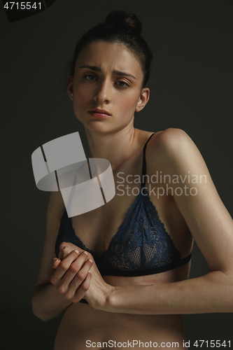 Image of Half-length portrait of young sad woman on dark studio background