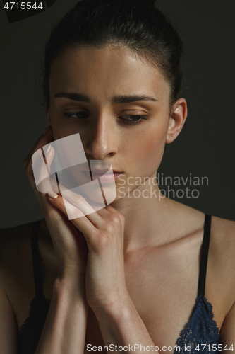 Image of Half-length portrait of young sad woman on dark studio background