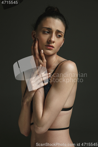 Image of Half-length portrait of young sad woman on dark studio background