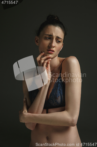 Image of Half-length portrait of young sad woman on dark studio background