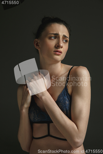 Image of Half-length portrait of young sad woman on dark studio background