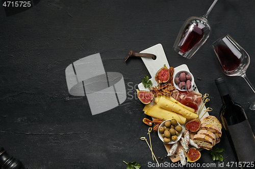 Image of Two glasses of red wine and cheese plate with fruit on the black stone