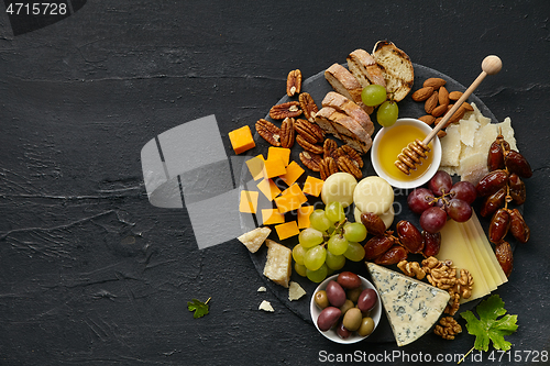 Image of Top view of tasty cheese plate with fruit on the black stone