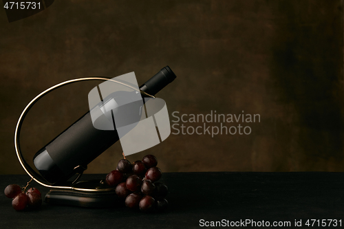 Image of Front view of tasty grapes plate with the wine bottle on dark studio background