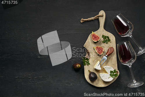 Image of Two glasses of red wine and a tasty cheese plate on a wooden kitchen plate.
