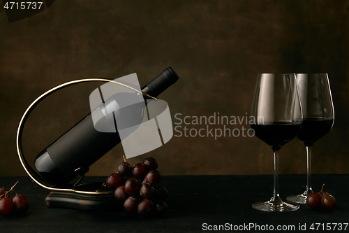 Image of Front view of tasty grapes plate with the wine bottle on dark studio background