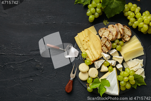 Image of Top view of tasty cheese plate with fruit on the black stone