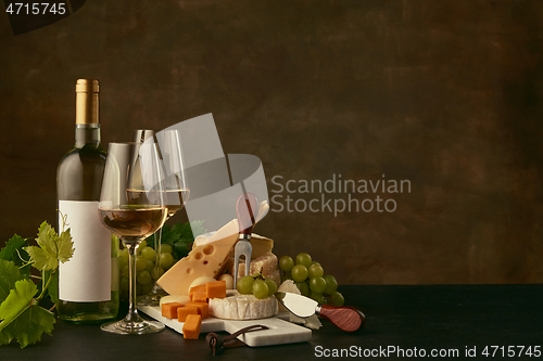 Image of Front view of tasty cheese plate with the wine bottle on dark studio background