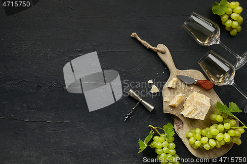 Image of Two glasses of white wine and a tasty cheese plate on a wooden kitchen plate.