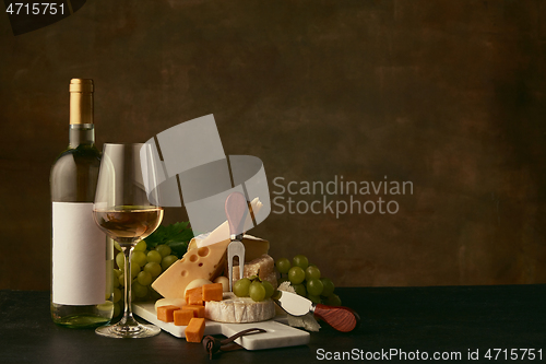 Image of Front view of tasty cheese plate with the wine bottle on dark studio background