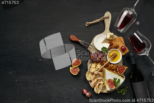 Image of Two glasses of red wine and cheese plate with fruit on the black stone