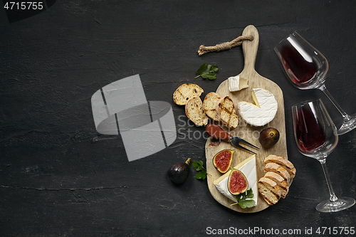 Image of Two glasses of red wine and cheese plate with fruit on the black stone