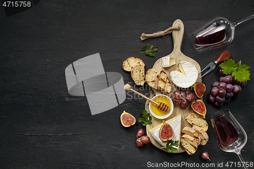 Image of Two glasses of red wine and cheese plate with fruit on the black stone